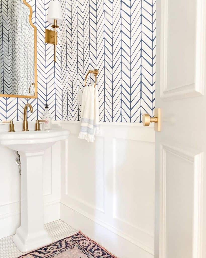 Bright bathroom with blue and white chevron wallpaper, pedestal sink, and gold accents.