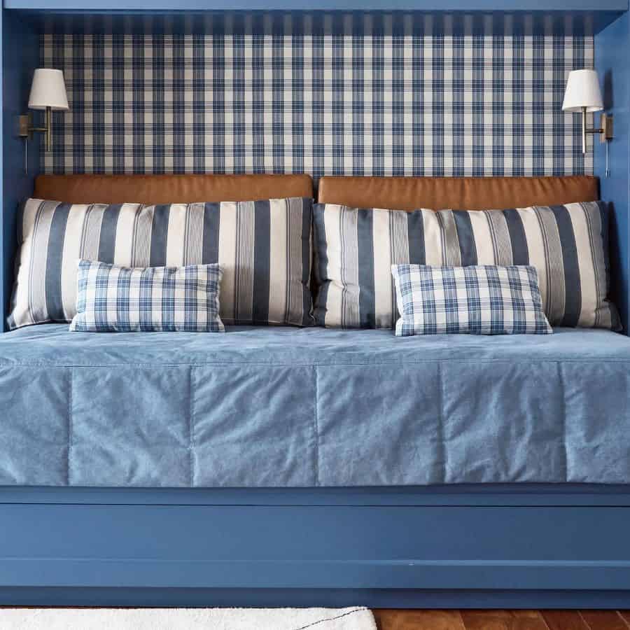 Cozy blue bedroom with plaid wallpaper, striped pillows, and leather accents for a classic, tailored look.