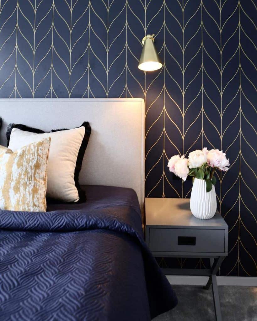 Elegant navy bedroom with gold-accented wallpaper, a modern bedside table, and a cozy bed adorned with chic pillows.