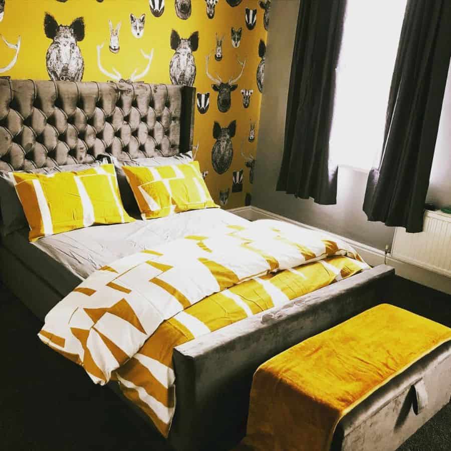 Bedroom with a plush bed, yellow bedding and gray accents, animal-patterned wallpaper, and dark curtains