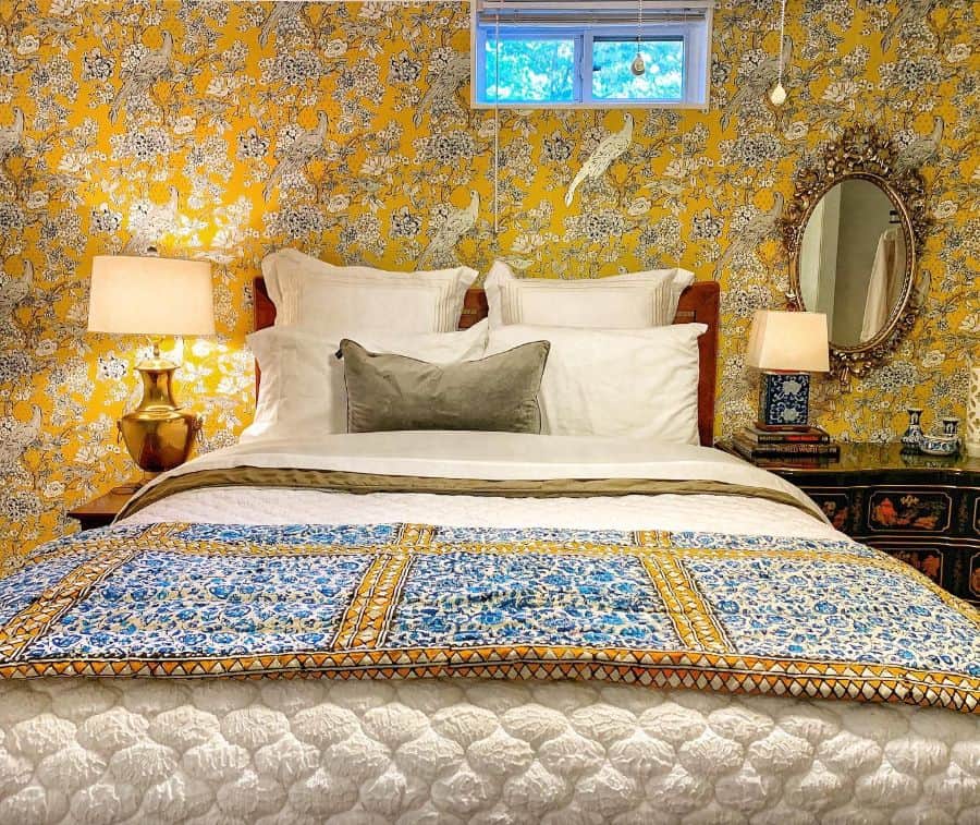 Cozy bedroom with floral wallpaper, a plush bed, ornate mirror, and warm yellow lighting from table lamps