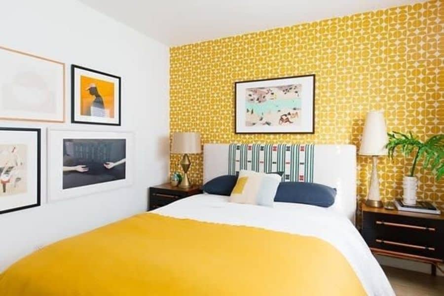 Bedroom with a vibrant yellow accent wall, a patterned headboard, framed artworks, and lamps adorning side tables
