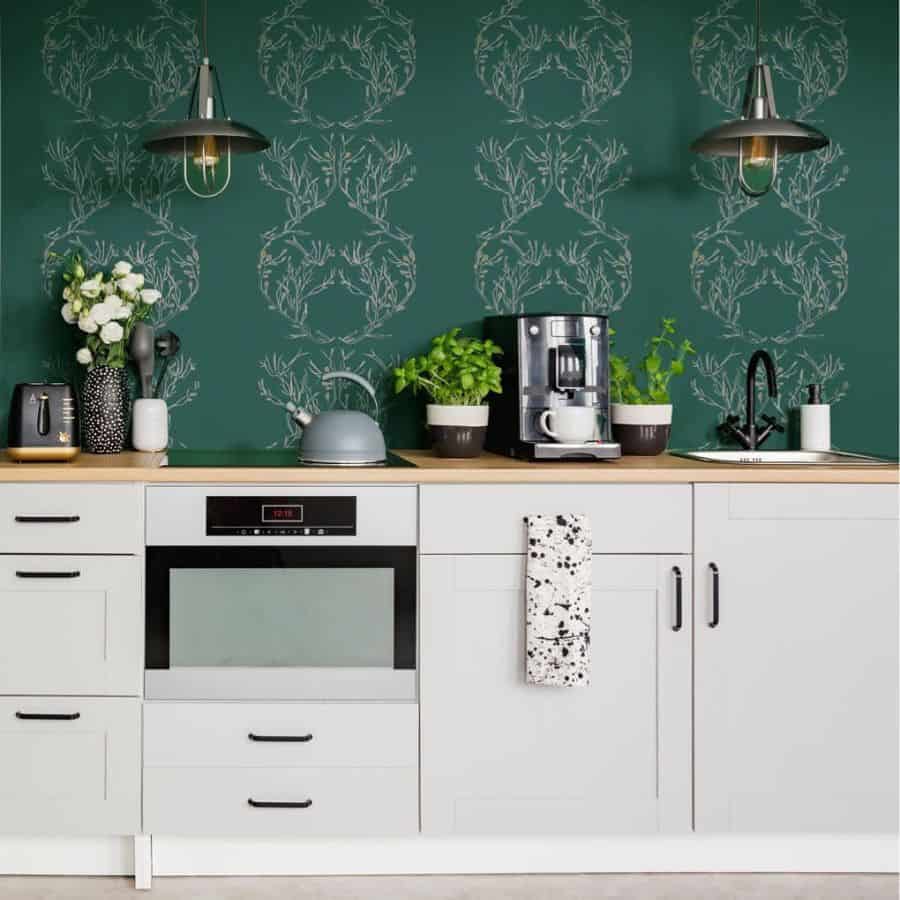 Modern kitchen with green wallpaper white cabinets wooden countertop and black pendant lights.