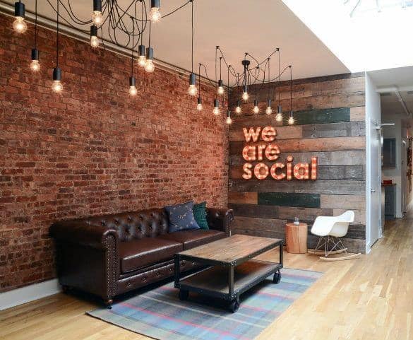 Warm industrial office lounge with brick wall, leather sofa, and We Are Social sign.