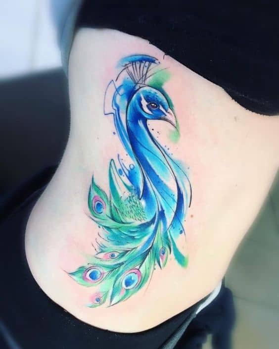 Watercolor-style peacock tattoo on the ribcage, featuring vibrant blue and green hues with delicate brushstroke effects and detailed feathers.