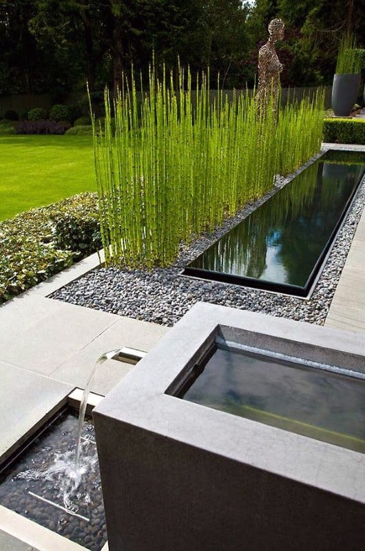 Modern garden with sleek water features, bamboo plants, pebbles, and manicured lawn.