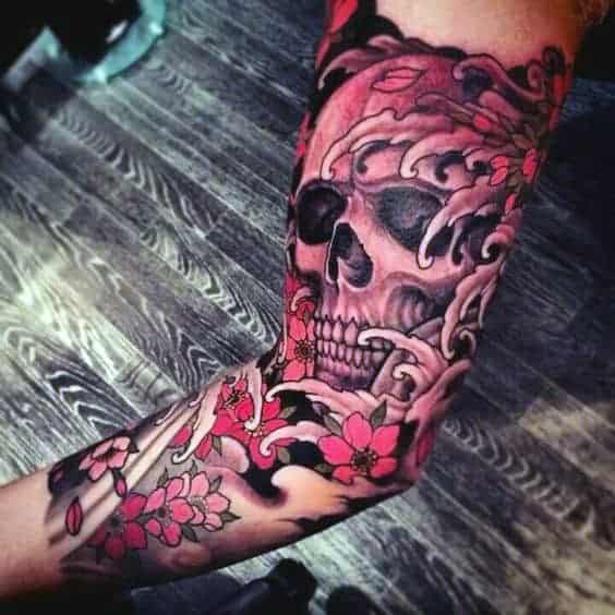 Arm tattoo featuring a skull with red floral and smoke designs on a wooden floor background