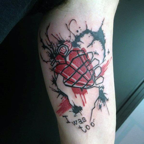 Tattoo of a red heart-shaped grenade with black ink splatters and the words “I was too…” below, inspired by *American Idiot* artwork.