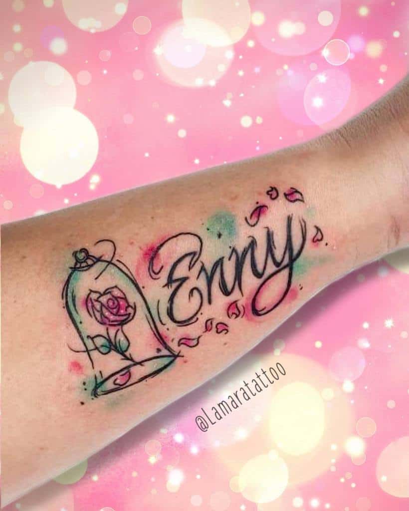 A vibrant watercolor tattoo featuring the Beauty and the Beast rose inside a glass dome, with the name "Enny" elegantly scripted beside it