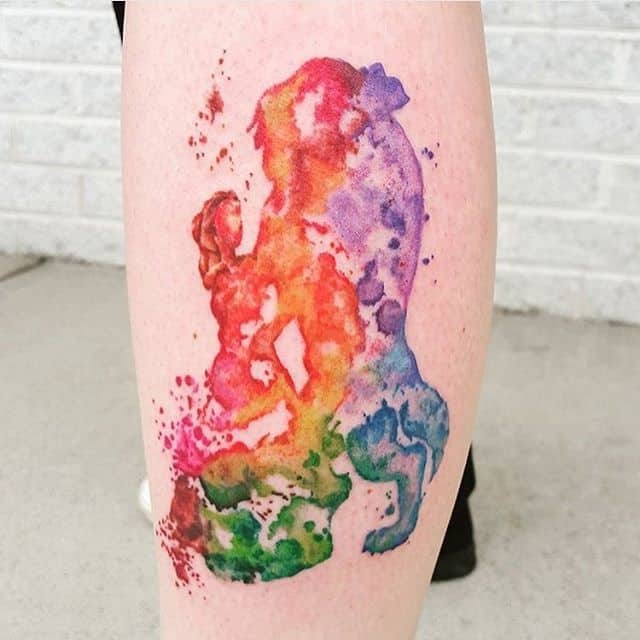 Abstract watercolor-style tattoo of Belle and the Beast in a vibrant rainbow color palette, blending splashes of red, orange, green, and blue.