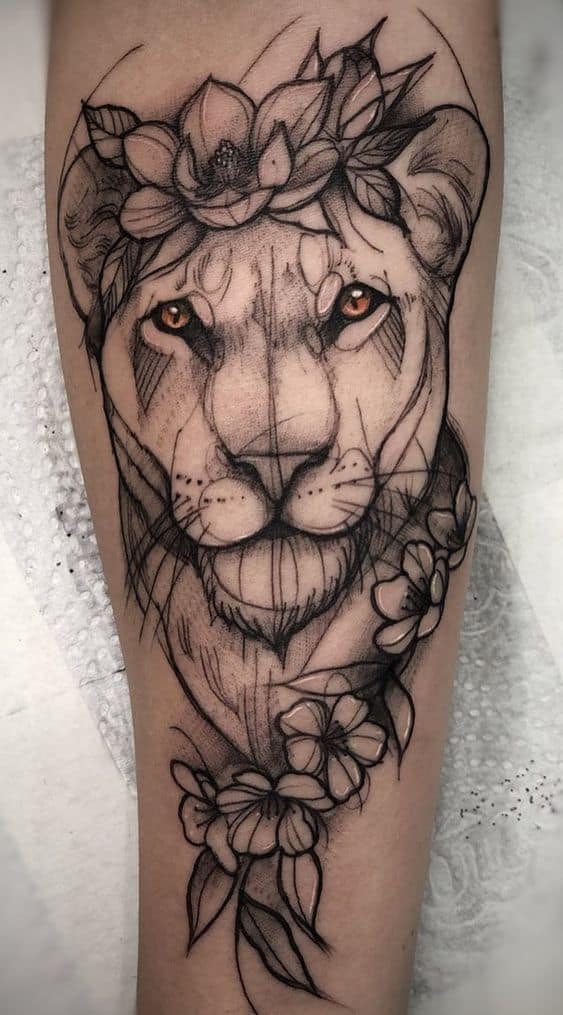 Detailed lioness tattoo on the forearm, featuring bold sketch-style lines, floral elements, and striking golden eyes for a fierce yet elegant look.
