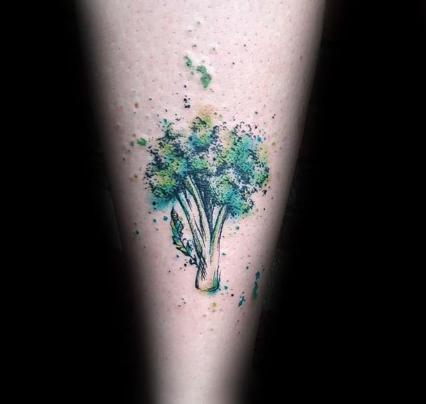Watercolor-style broccoli tattoo on the forearm, featuring splashes of green and blue ink for a vibrant and artistic design.