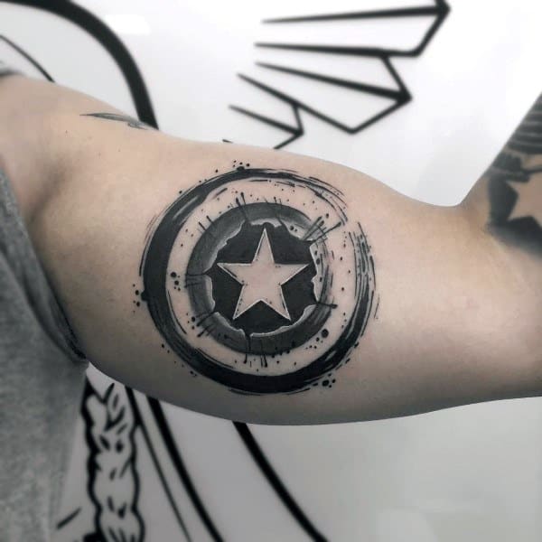 Bold black ink tattoo on inner bicep featuring a distressed circular shield with a central star, inspired by Captain America's emblem.