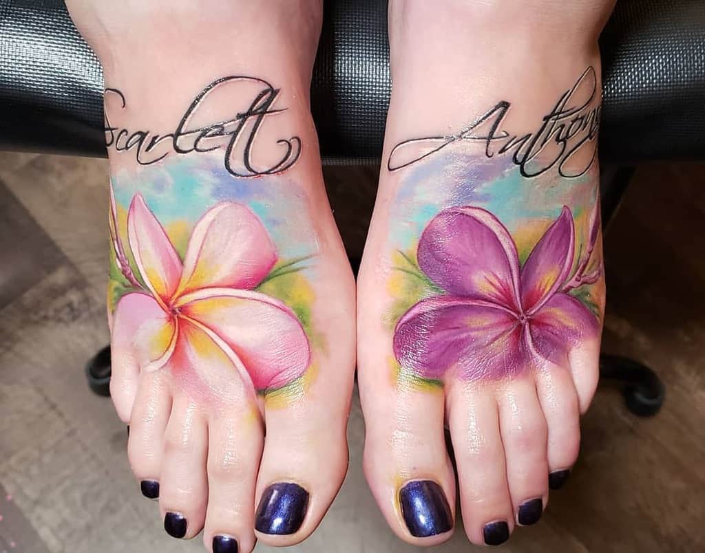 Feet tattoos with colorful plumeria flowers and cursive writing