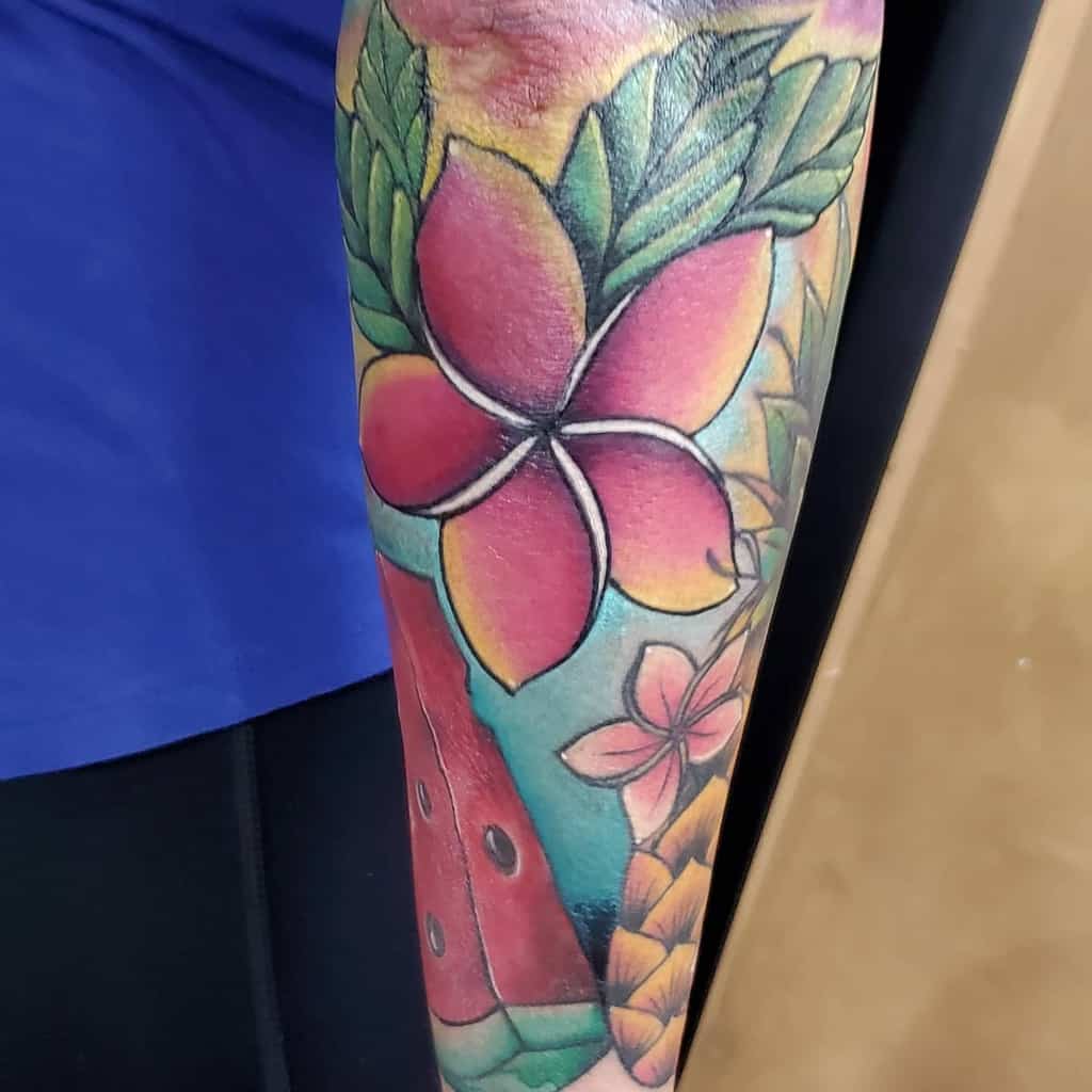 Colorful tattoo featuring plumeria flowers, a watermelon slice, and leaves on an arm