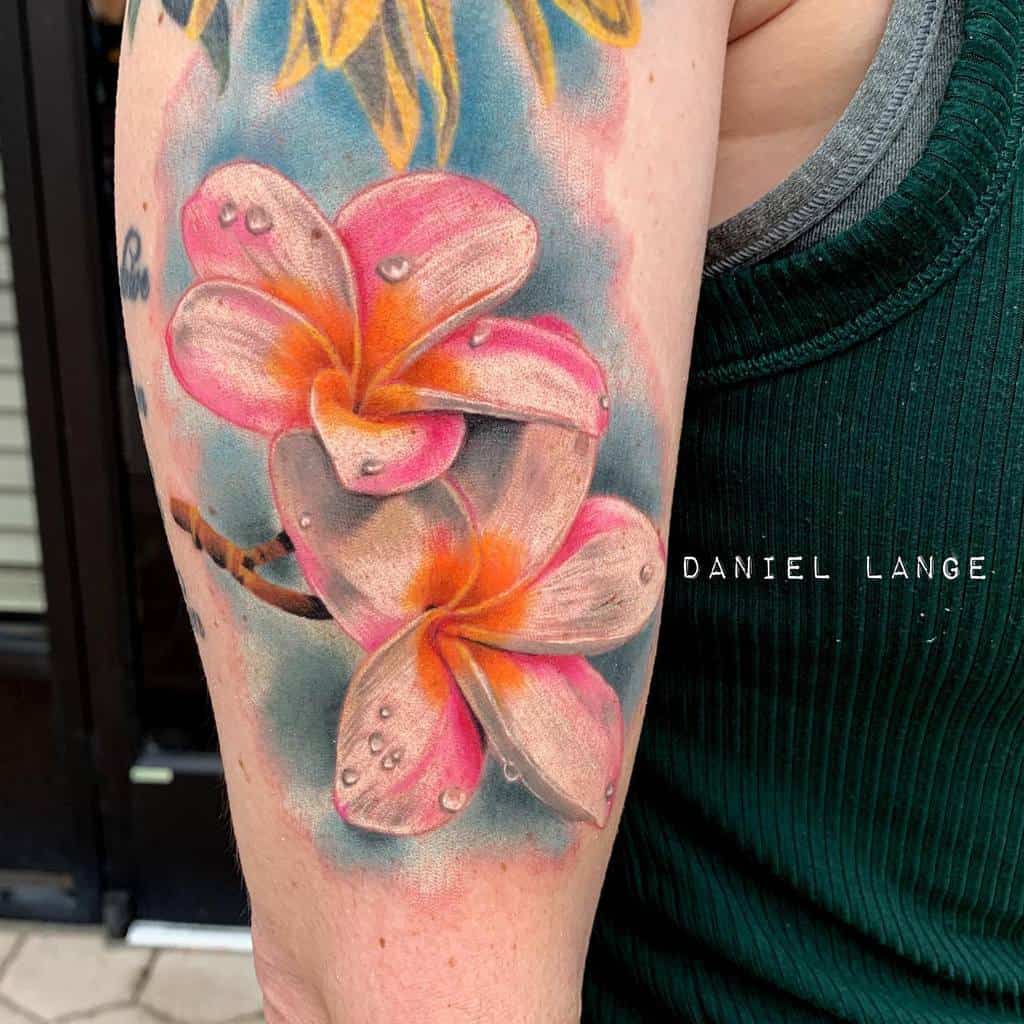 Vivid Plumeria tattoo in a watercolor style, featuring soft pink and orange hues with lifelike water droplets, set against a dreamy blue background