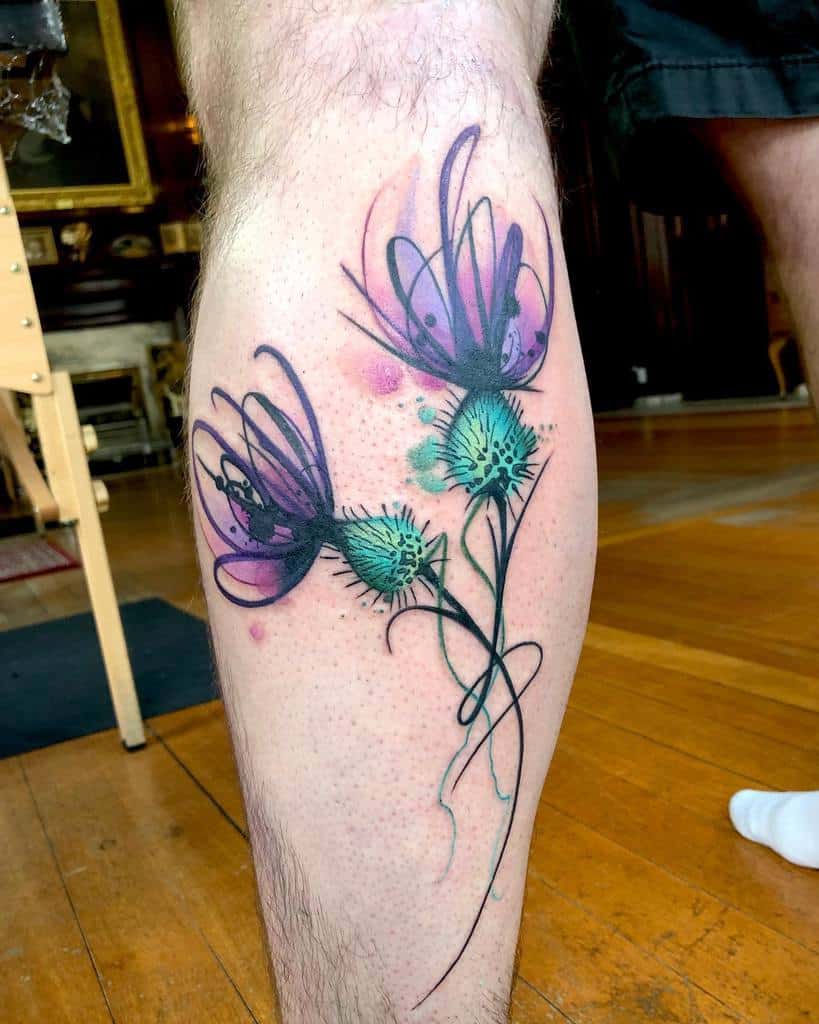 A vibrant thistle tattoo graces a person's calf, adding a burst of color to their skin