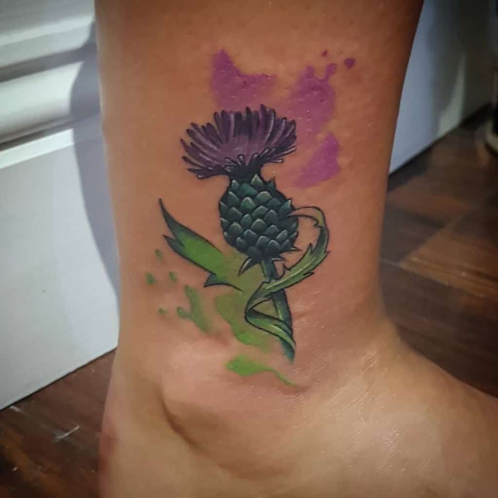 A vibrant tattoo of a thistle graces the ankle, its purple and green ink accents bringing this iconic flower to life with exquisite detail