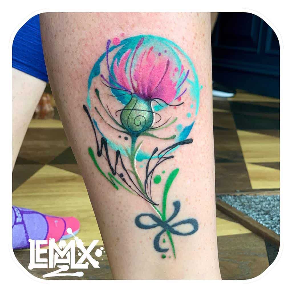 A tattoo of a delicate pink thistle with abstract lines and watercolor style adorns a person's leg