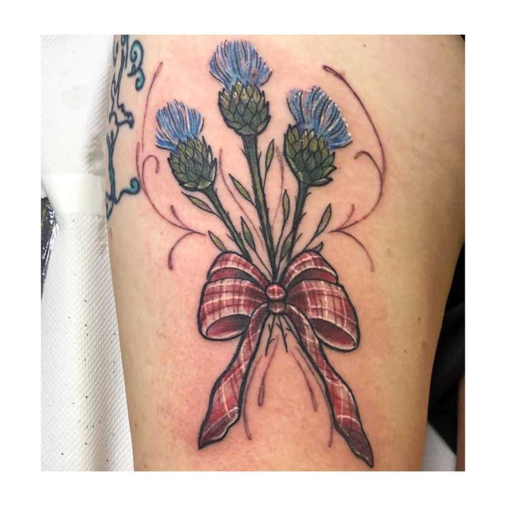 A tattoo of delicate thistle flowers gracefully bound with a patterned ribbon adorns the skin