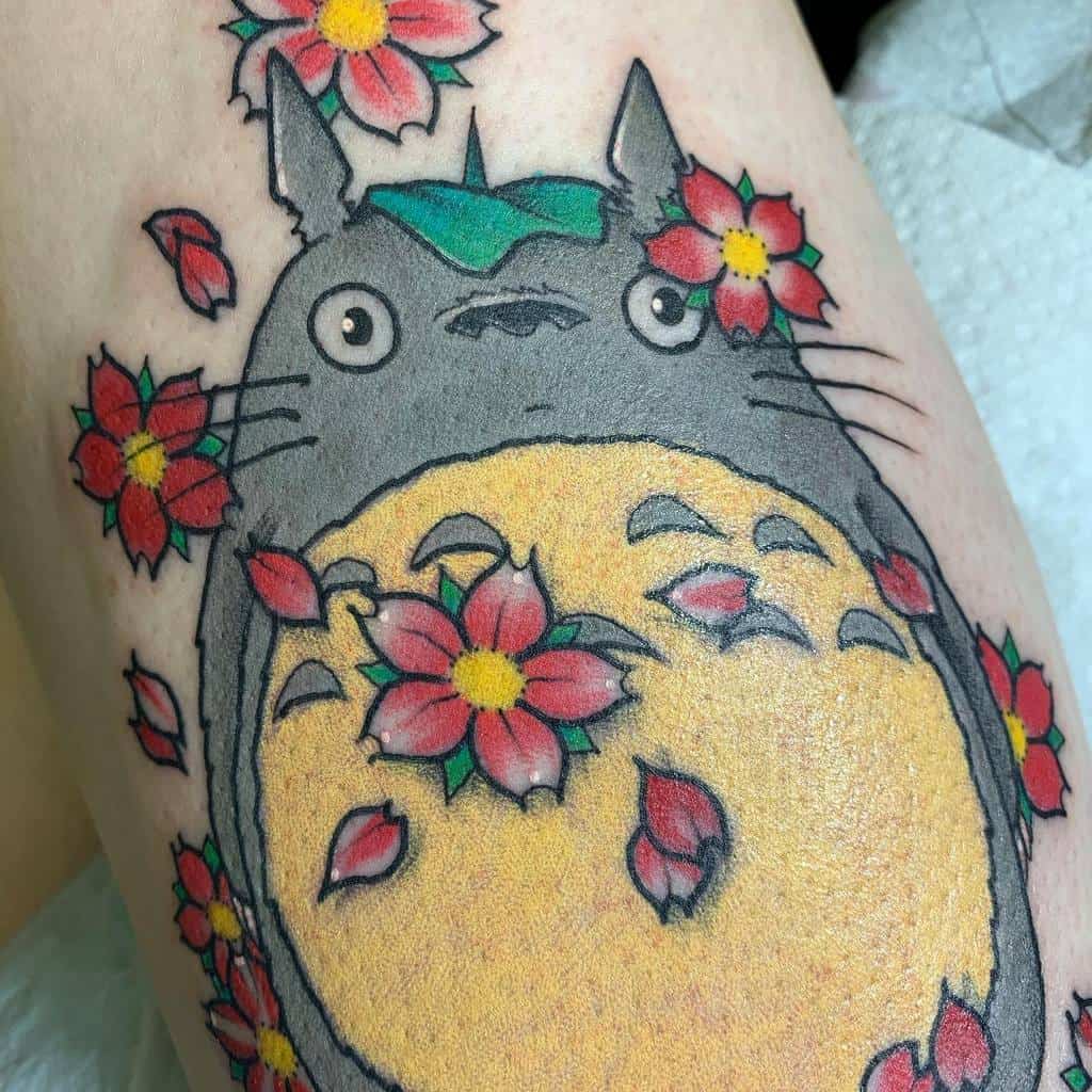 Tattoo of a cartoon creature surrounded by red flowers and petals