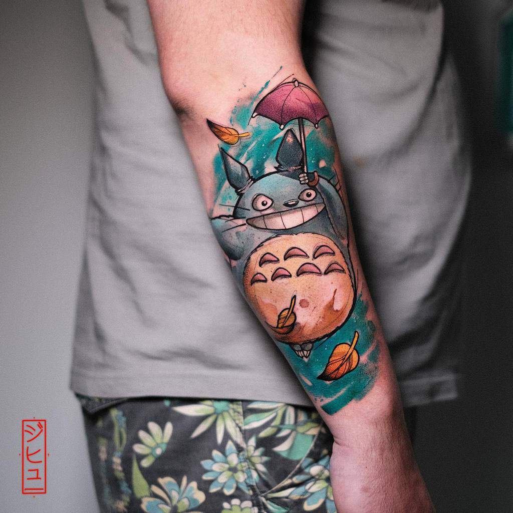 Colorful cartoon creature tattoo on forearm with umbrella and leaves
