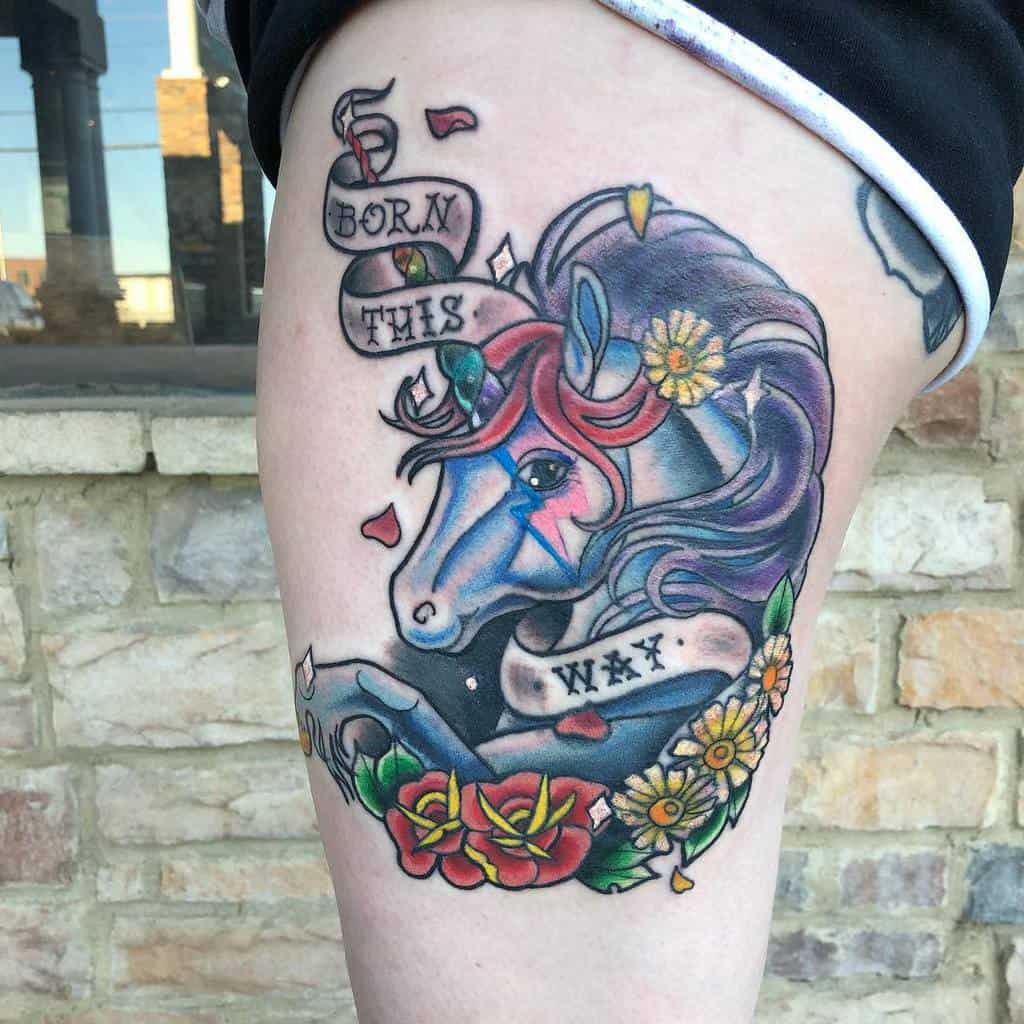 Colorful unicorn tattoo with "Born This Way" banner and flowers on thigh