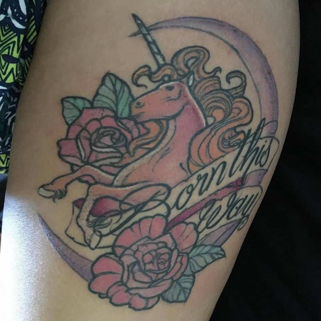 Tattoo of a unicorn with "Born this way" text, surrounded by roses and a crescent moon