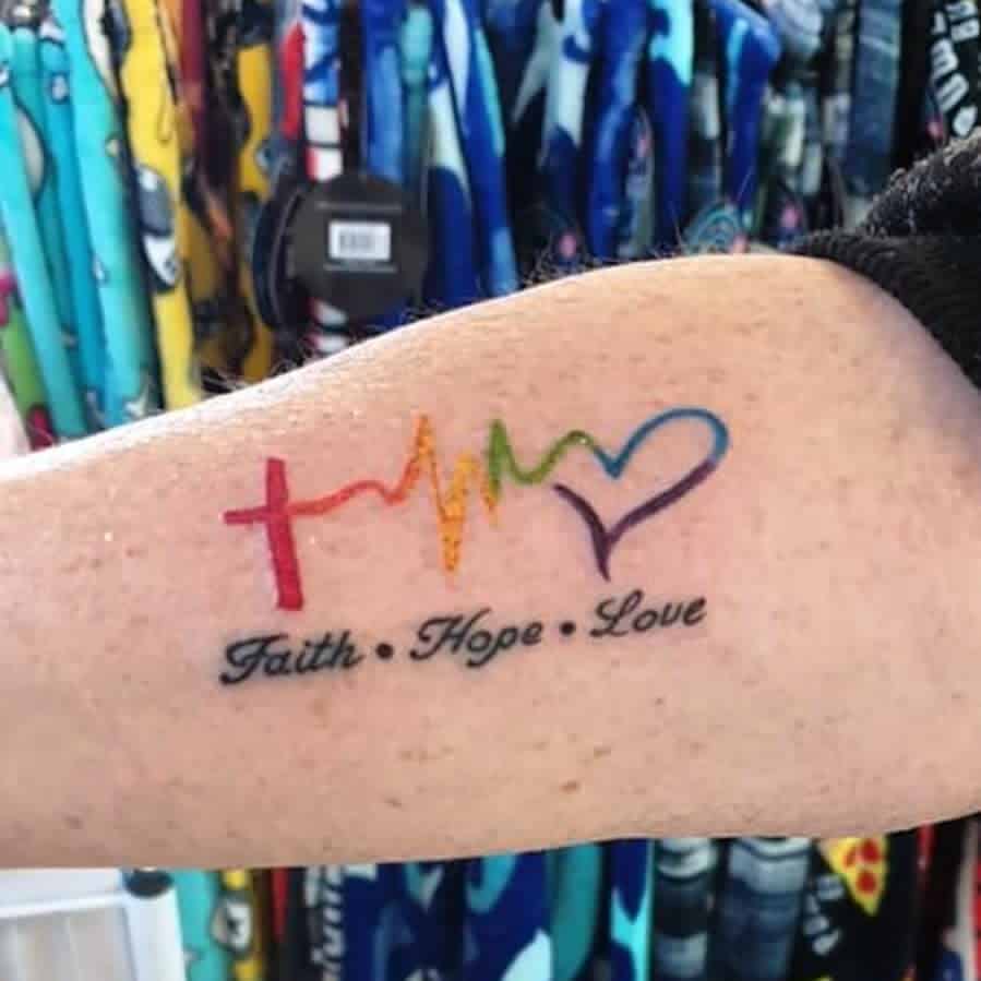 Tattoo of a cross, heartbeat, and heart in rainbow colors with text "Faith Hope Love" on an arm