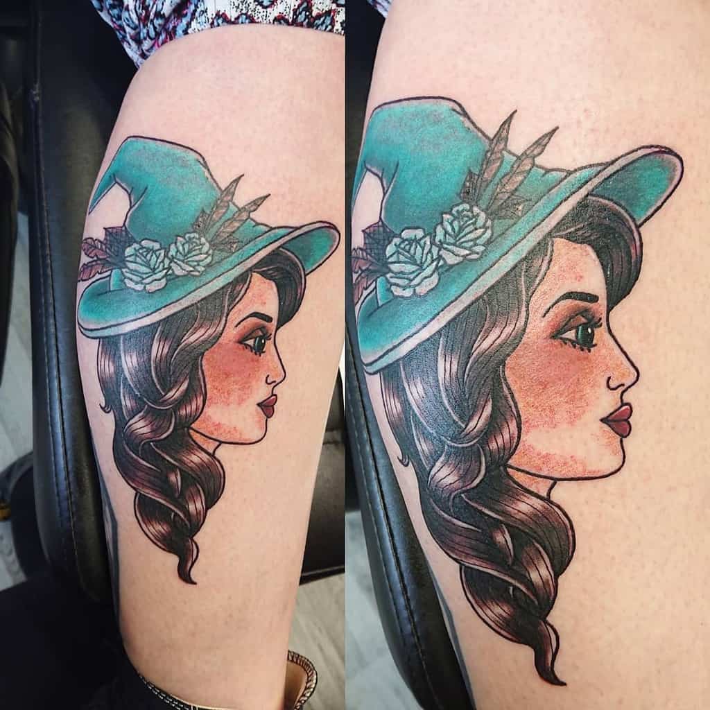 Tattoo of a gypsy woman in a green hat with flowers, brown hair, and a profile view on a leg