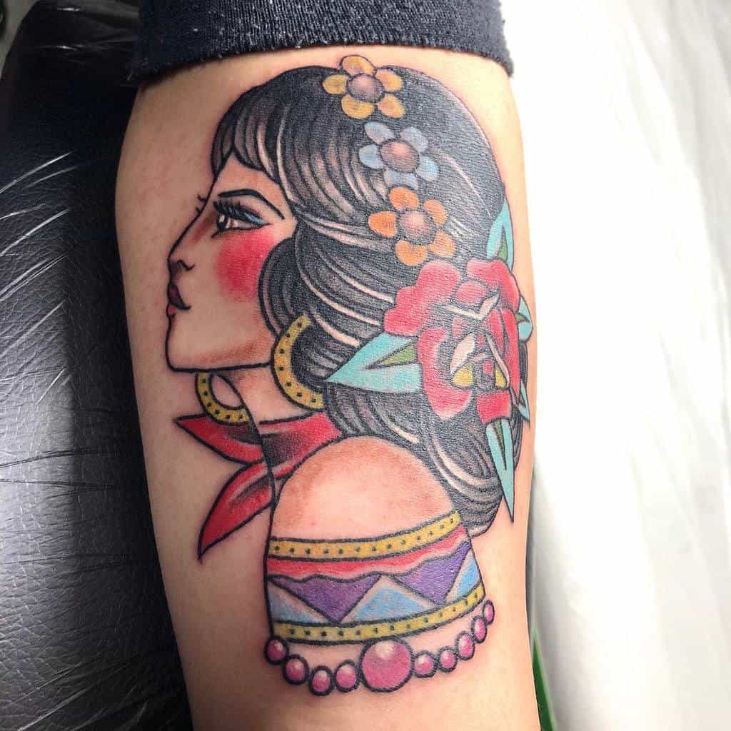 A vibrant tattoo of a gypsy woman in profile, adorned with flowers and an intricately patterned dress, graces the arm