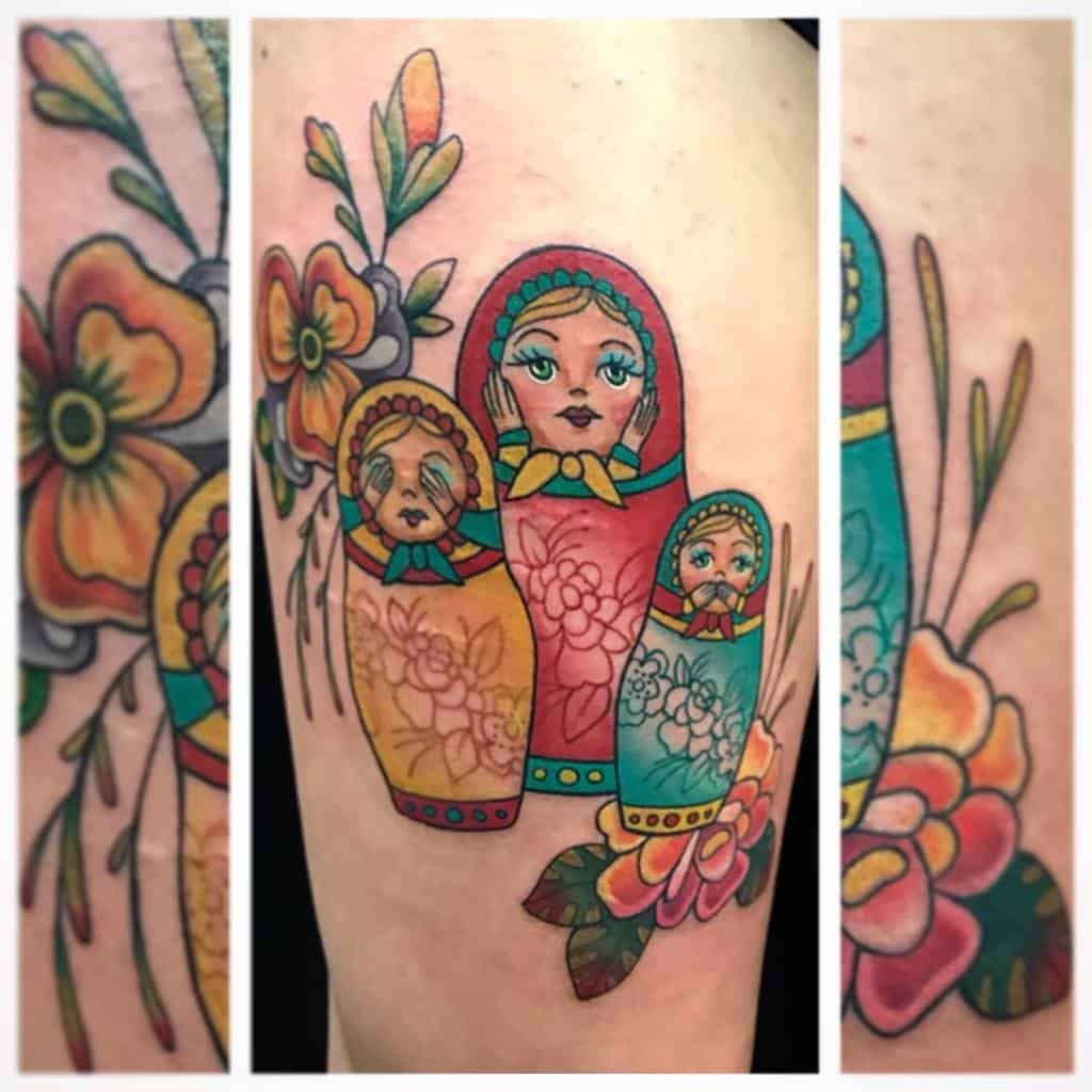 Colorful tattoo of three Matryoshka dolls in red, yellow, and teal, each representing 'Hear No Evil, See No Evil, Speak No Evil,' surrounded by vibrant floral designs