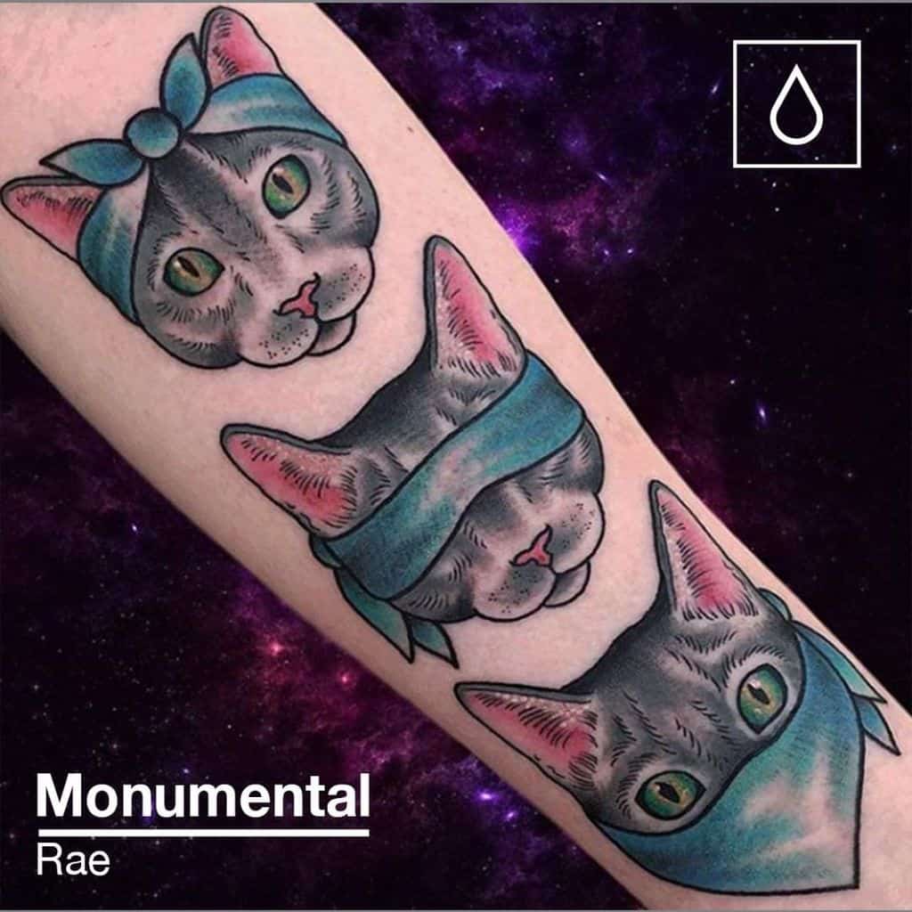 Forearm tattoo of three gray cats, each representing 'Hear No Evil, See No Evil, Speak No Evil,' with vibrant blue accessories and a cosmic background