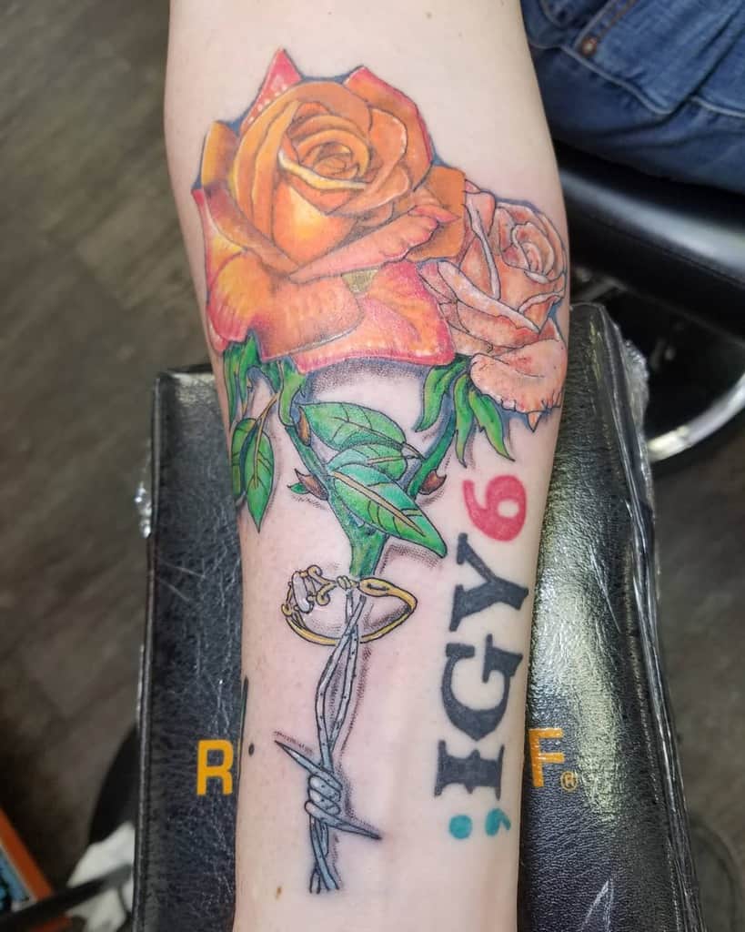 Forearm tattoo featuring vibrant orange roses, barbed wire, and the text 'IGY6' with a blue semicolon and red 6