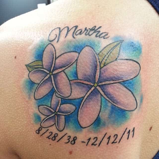 Tattoo of three Jasmine flowers with text "Martha" and dates on shoulder