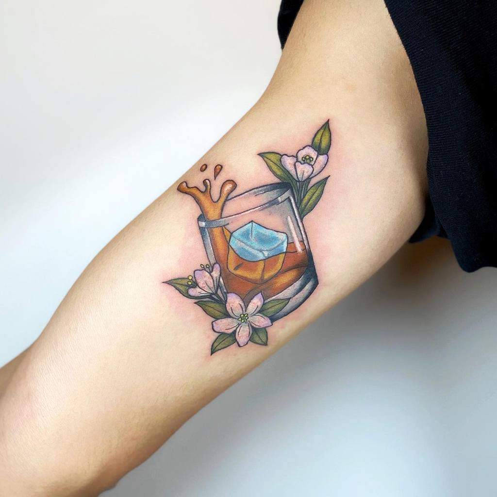 Tattoo of a splashing drink in a glass with jasmine flowers and leaves on an arm