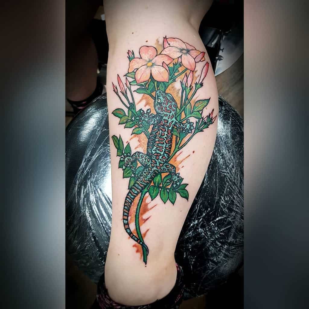 Colored tattoo of a lizard with flowers and leaves on an upper leg