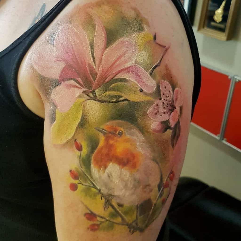 A vibrant tattoo of magnolia flowers and a bird graces the upper arm, creating an eye-catching masterpiece