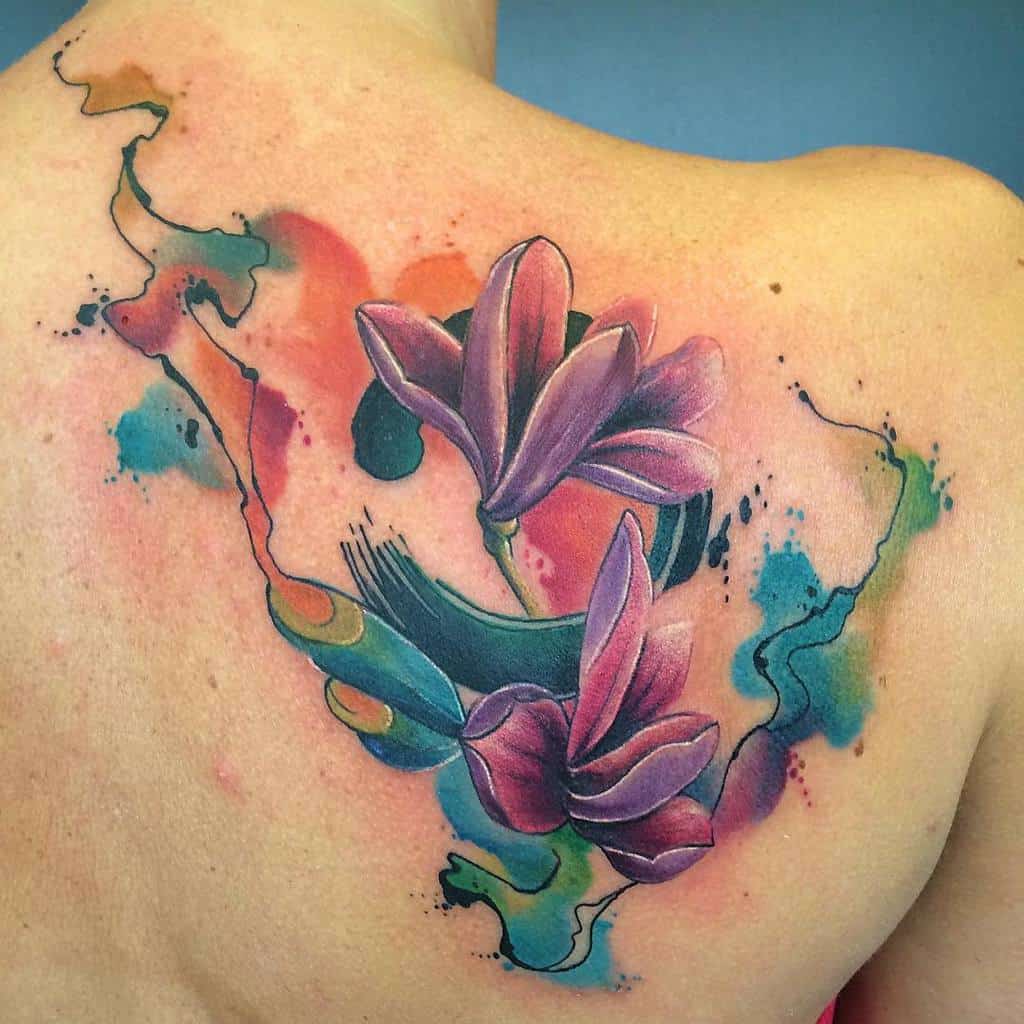 A vibrant abstract magnolia flower tattoo graces the shoulder with a stunning watercolor effect