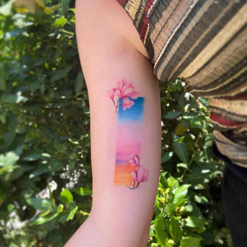 A colorful tattoo of magnolia flowers and a sunset graces a person's arm