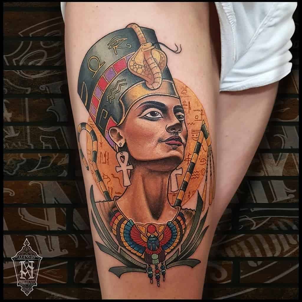 Colorful tattoo of an Egyptian queen with a headdress, ankh symbols, and intricate designs on the upper arm