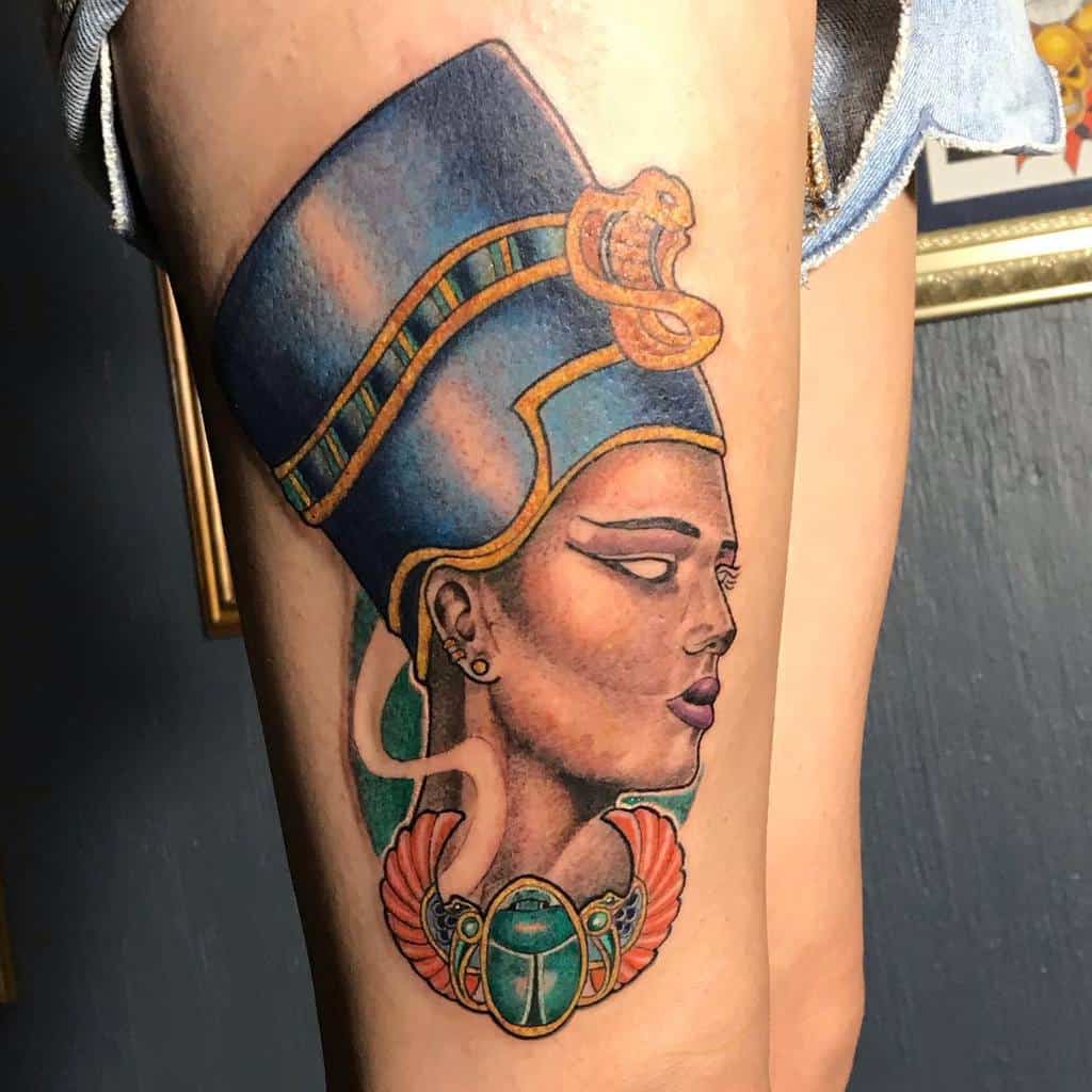 Colorful tattoo of an Egyptian queen profile with a headdress and scarab on an upper arm