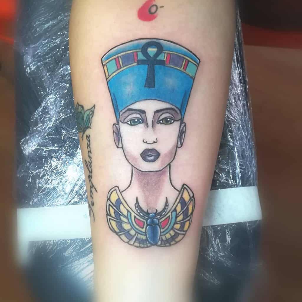 Tattoo of an Egyptian queen wearing a blue headdress and a jeweled necklace on a forearm