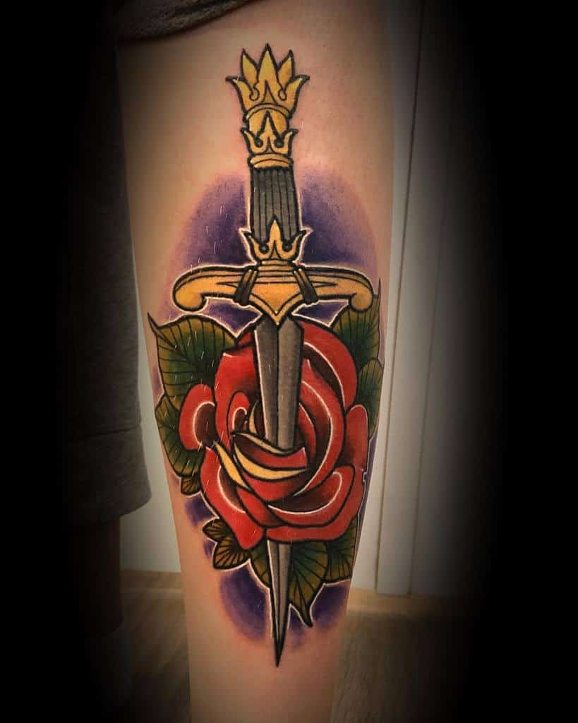 Tattoo of a dagger through a rose with green leaves and a purple background