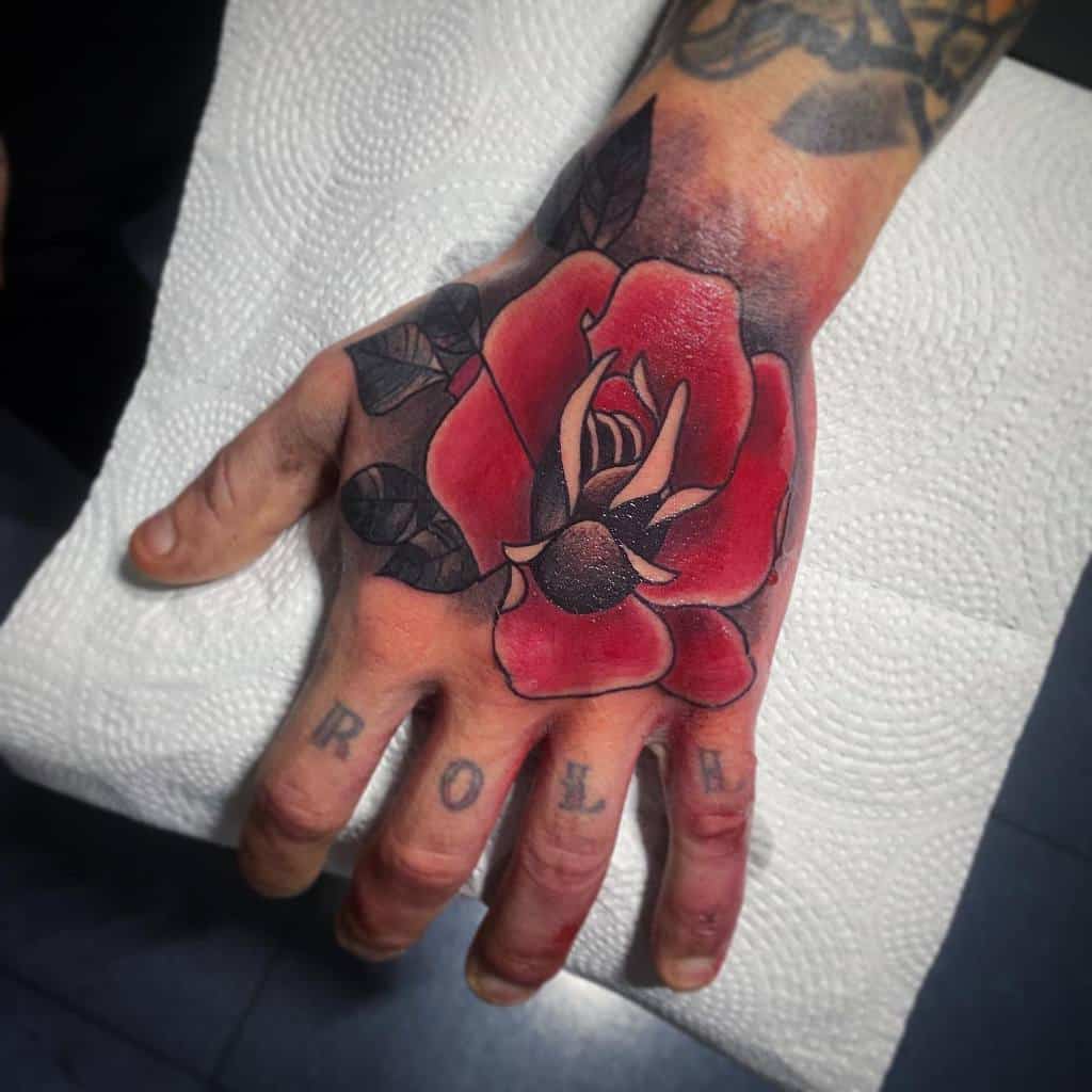 Hand tattoo of a large red rose with black leaves and letters on fingers