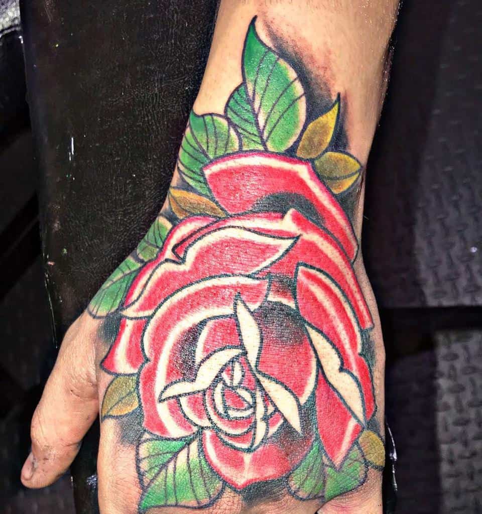 A vibrant hand tattoo showcasing a colorful rose in deep red, surrounded by lush green leaves