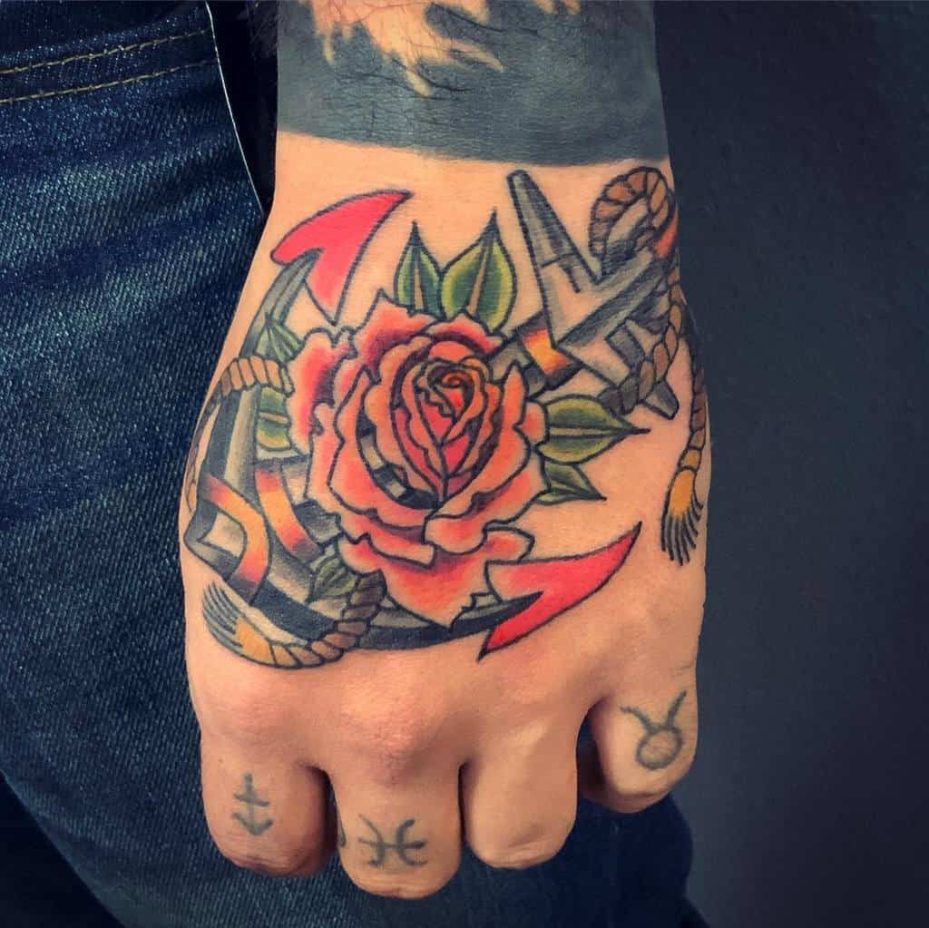 A beautifully detailed tattoo of a rose intertwined with an anchor adorns the person's hand, complemented by finger tattoos featuring intriguing symbols