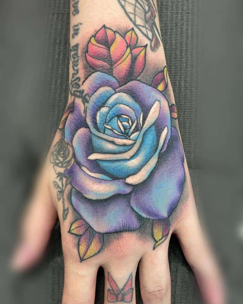 Hand with a colorful blue and pink rose tattoo and small designs