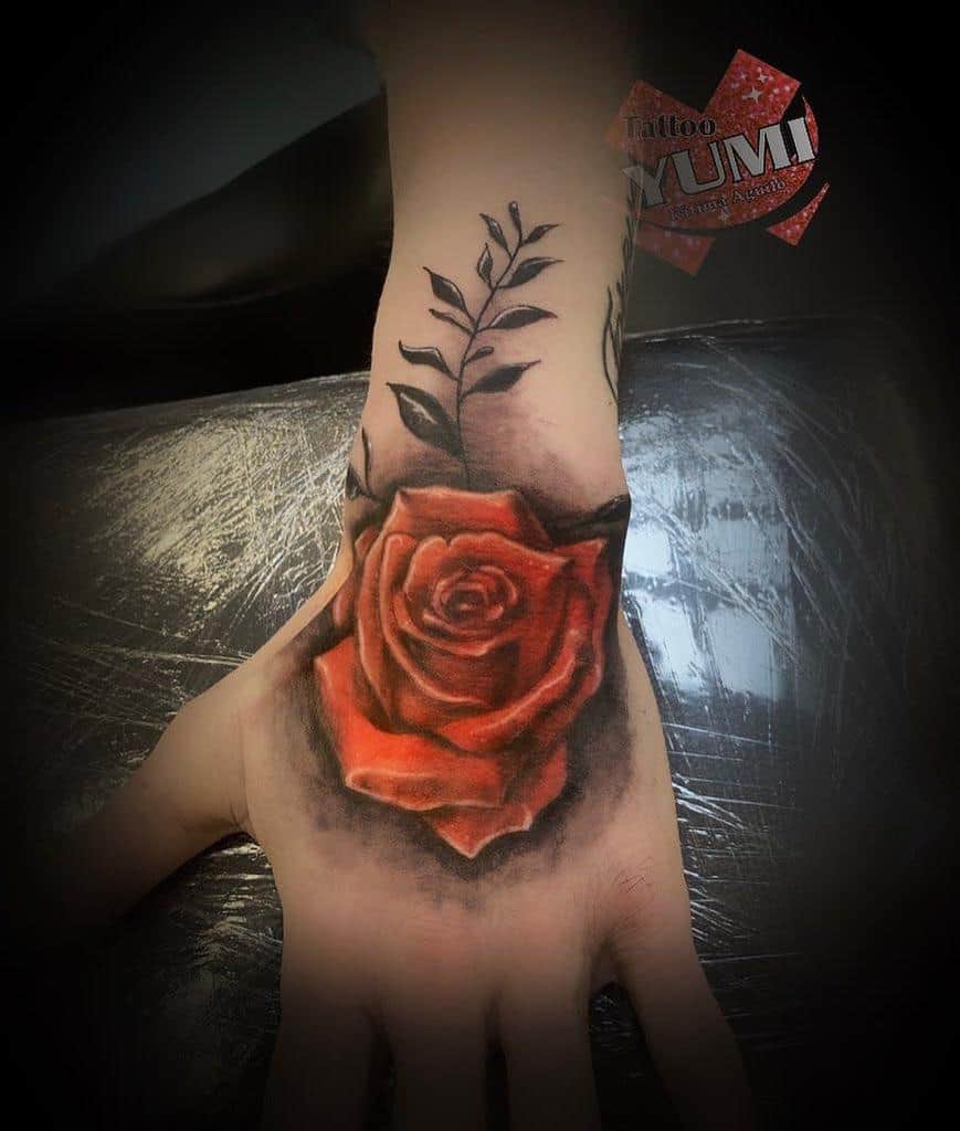 Hand tattoo of a red rose with black leaves on the wrist
