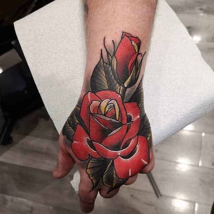 Red rose tattoo on the back of a person's hand with green leaves